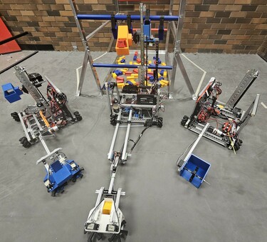 Three robots complete with wheels and crane mechanisms sit on a classroom floor.