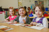 A group of young students sit at a desk together and smile at the camera.