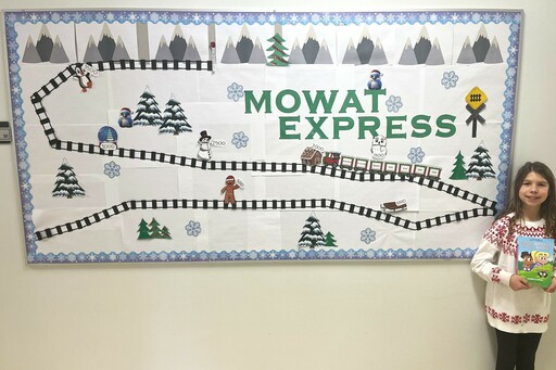 Elizabeth Kuzyk, a Grade 4 student at James Mowat Elementary, stands beside a bulletin board displaying the school’s Mowat Express reading challenge.