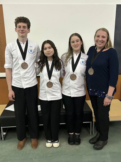 Bev Facey Community High Chef and Culinary Teacher Jennifer Steele-Watts stands next to Bev Facey students Levi Burdett and Kara Mah—along with their teammate Danica Edwards from Salisbury Composite High—who won bronze for the 2025 HSCC.