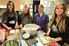 Four students stand within a classroom at a desk covered in ingredients for making sushi rolls.