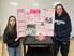 Two students stand in front of a white board holding up a poster board filled with text boxes inlaid into hot pink construction paper. There are various images related to solar energy.